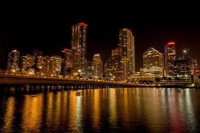 Illuminated buildings by river against sky at night