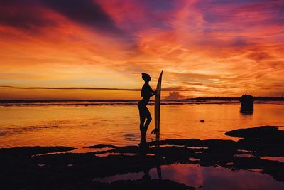 Silhouette woman standing on beach against sunset sky