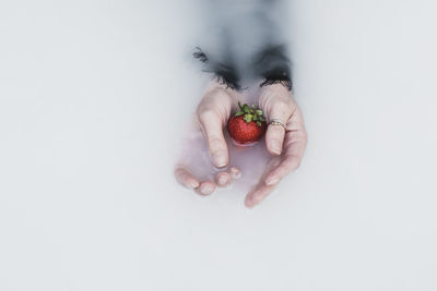 Cropped hand of woman with strawberry in milk