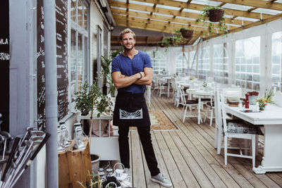Full length portrait of male owner with arms crossed standing in restaurant