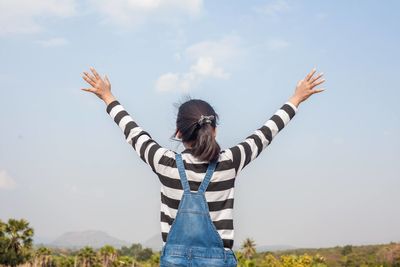 Rear view of woman with arms raised against sky