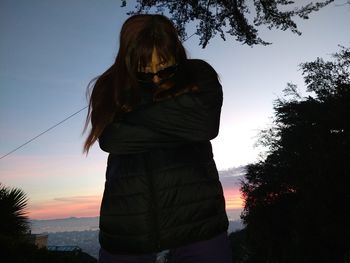 Woman standing by tree against sky during sunset