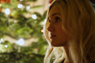 Close-up of thoughtful young woman with christmas tree in background