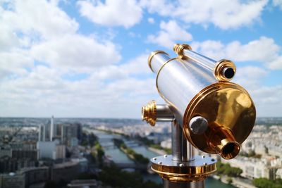 Close-up of coin-operated binoculars with cityscape in background against sky