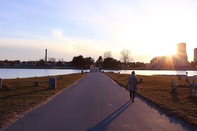 Rear view of woman walking on road in city against sky during sunset