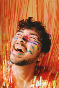 Queer young man smiling in colorful face paint in glowing curtains at a party