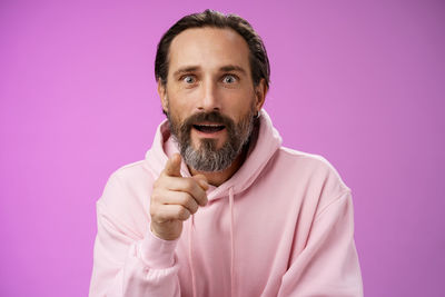 Surprised man pointing against purple background