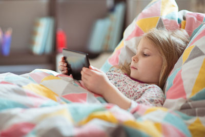 Cute girl using phone while lying on bed