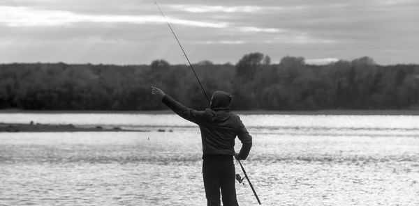 Rear view of man fishing on shore against sky