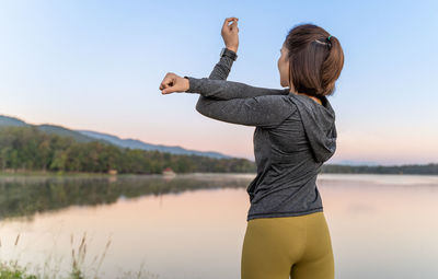 Young attractive woman stretching her arms and legs before her morning exercise at a local lake park