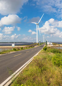 Wind turbines on field by road against sky