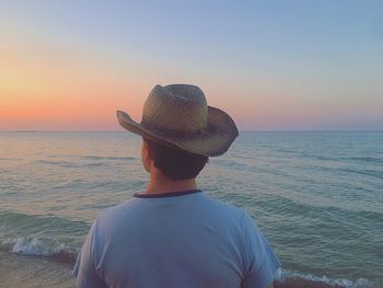 Man in hat looking at sea against sky