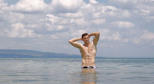 Young man in sea with hands behind head standing against sky