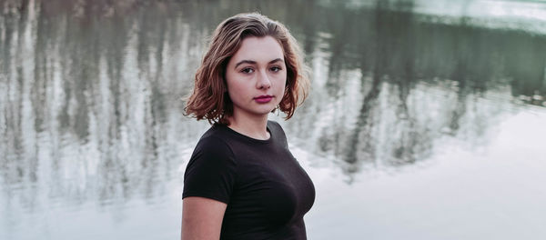 Portrait of beautiful woman standing against lake