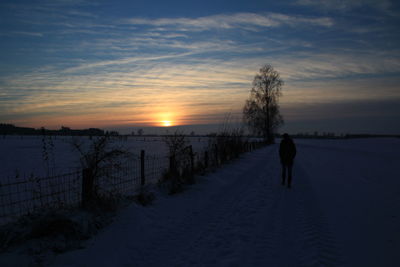 Rear view of woman on snow covered land during sunset