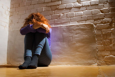 Low angle view of sad woman sitting against brick wall