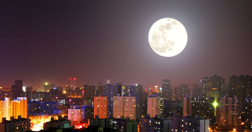 Full moon over illuminated buildings in city at night