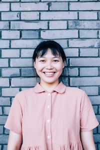 Portrait of a smiling young woman standing against brick wall