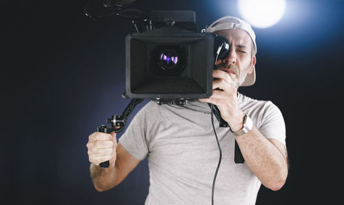 Man holding camera while standing against black background