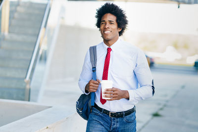 Smiling businessman holding disposable cup while walking