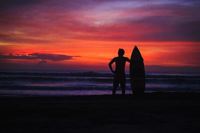 Silhouette friends standing on beach against sky during sunset