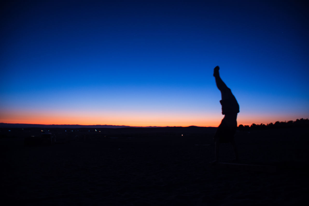SILHOUETTE MAN WITH ARMS RAISED STANDING ON BEACH AGAINST SKY DURING SUNSET