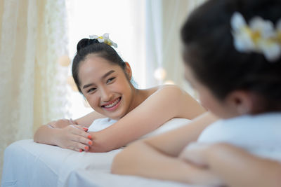 Young woman looking at friend while lying massage table in spa