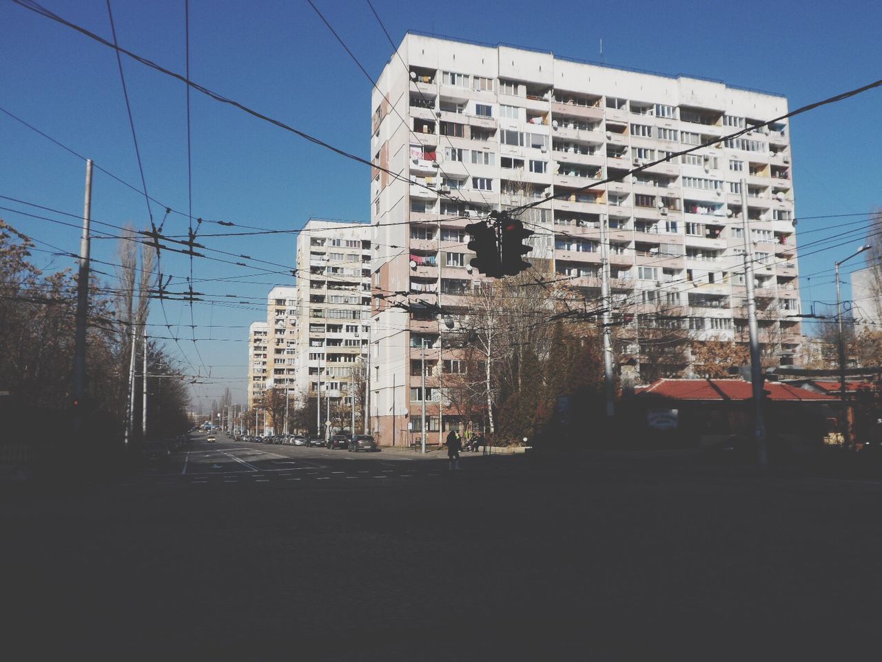 building exterior, built structure, architecture, city, transportation, car, outdoors, residential building, mode of transport, land vehicle, clear sky, road, power line, no people, sky, day, tree, electricity pylon