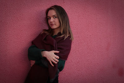 Portrait of young woman standing against pink wall