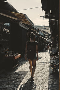 Woman walking on alley amidst buildings in city