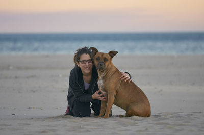 Portrait of woman with dog at beach during sunset