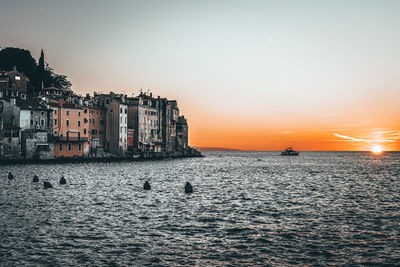 Sea by buildings against sky during sunset