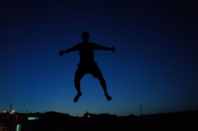 Low angle view of woman jumping against blue sky