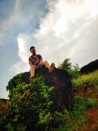 Low angle view of man sitting on rock against sky