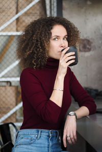 Young beautiful curly brunette woman drinking coffee while sitting at table in modern cafe.