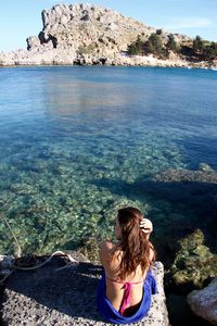 Rear view of woman standing on rock by sea against sky