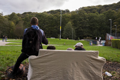 Rear view of man sitting on grass against sky