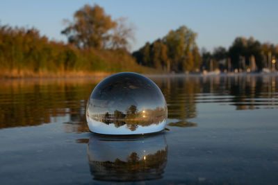 Close-up of crystal ball on lake against trees