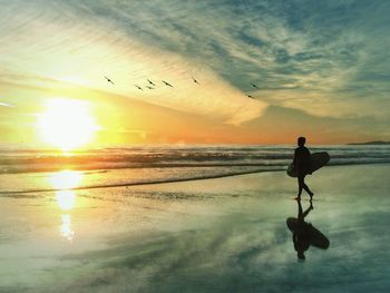 Silhouette woman standing on beach against sky during sunset