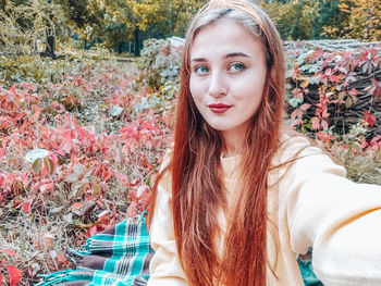 Smiling young woman taking selfie sitting on blanket in forest 