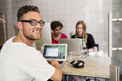 Portrait of happy young businessman with colleagues in background at creative office