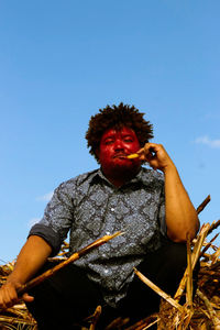 Low angle view of man eating sugarcane against clear sky