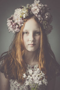 Portrait of teenage girl wearing flowers against gray background