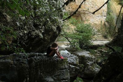 Side view of woman sitting on rock at forest