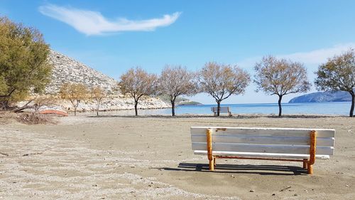 Empty bench in park by sea against sky