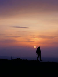 Silhouette man standing on field against sky during sunset