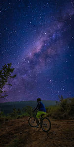 Man riding bicycle on field against sky at night