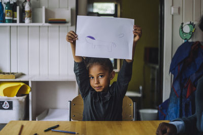 Portrait of student showing drawing on paper in day care center