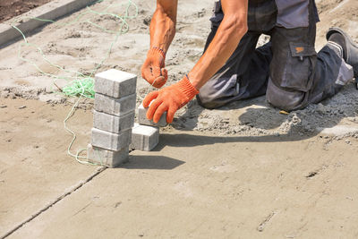 A worker on a sandy surface sets a level with stretched nylon thread for laying paving slabs on day.