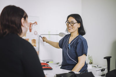 Happy mature doctor explaining organs to patient while pointing at chart in medical clinic